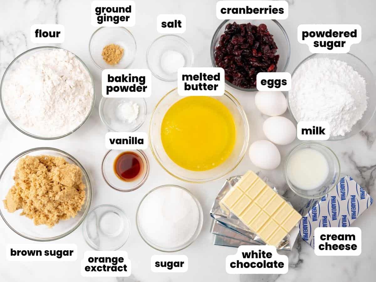 The ingredients needed to make starbucks copycat cranberry bliss bars, all measured into separate bowls and arranged on a marble counter. Key ingredients here include dried cranberries, white chocolate, and cream cheese.