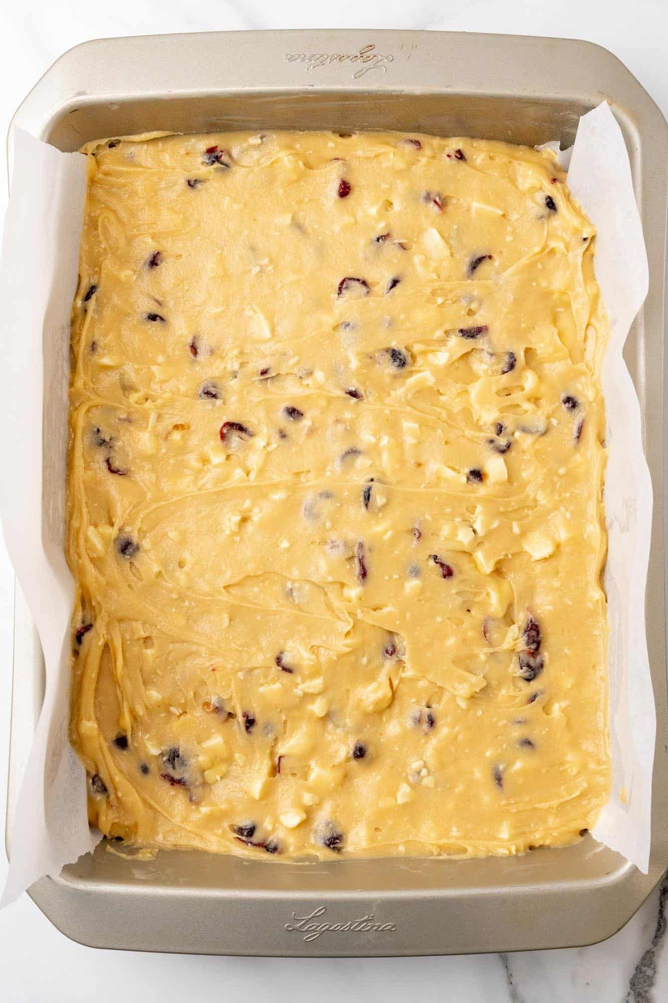 batter for cranberry bliss bars spread into a 9x13 inch pan that has been lined with parchment paper.