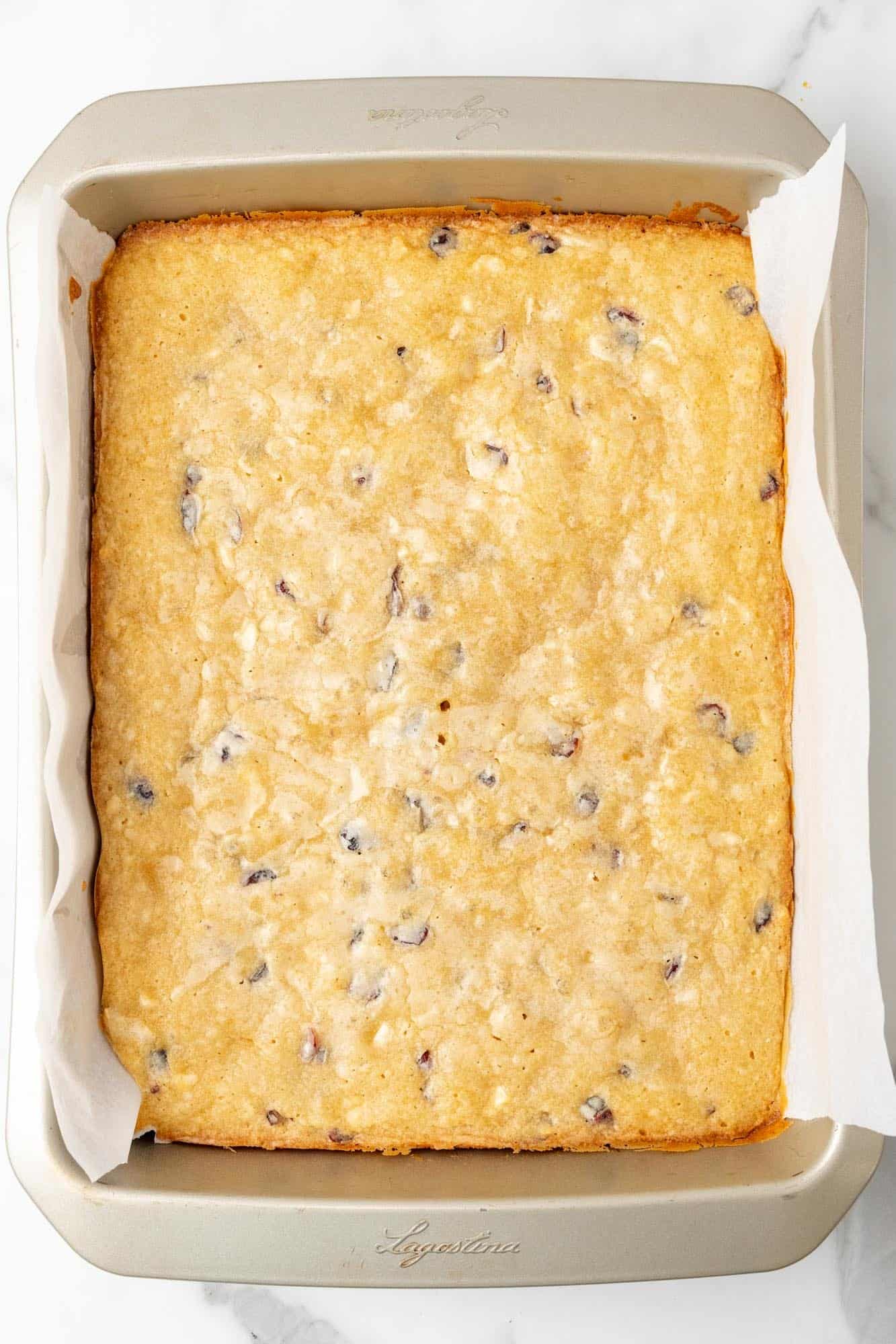 baked cranberry bliss bars in a pan with parchment paper.