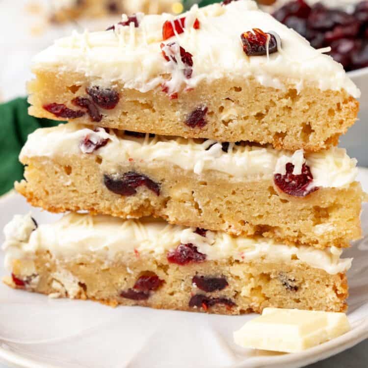 three triangle shaped cranberry bliss bars stacked on a white plate.