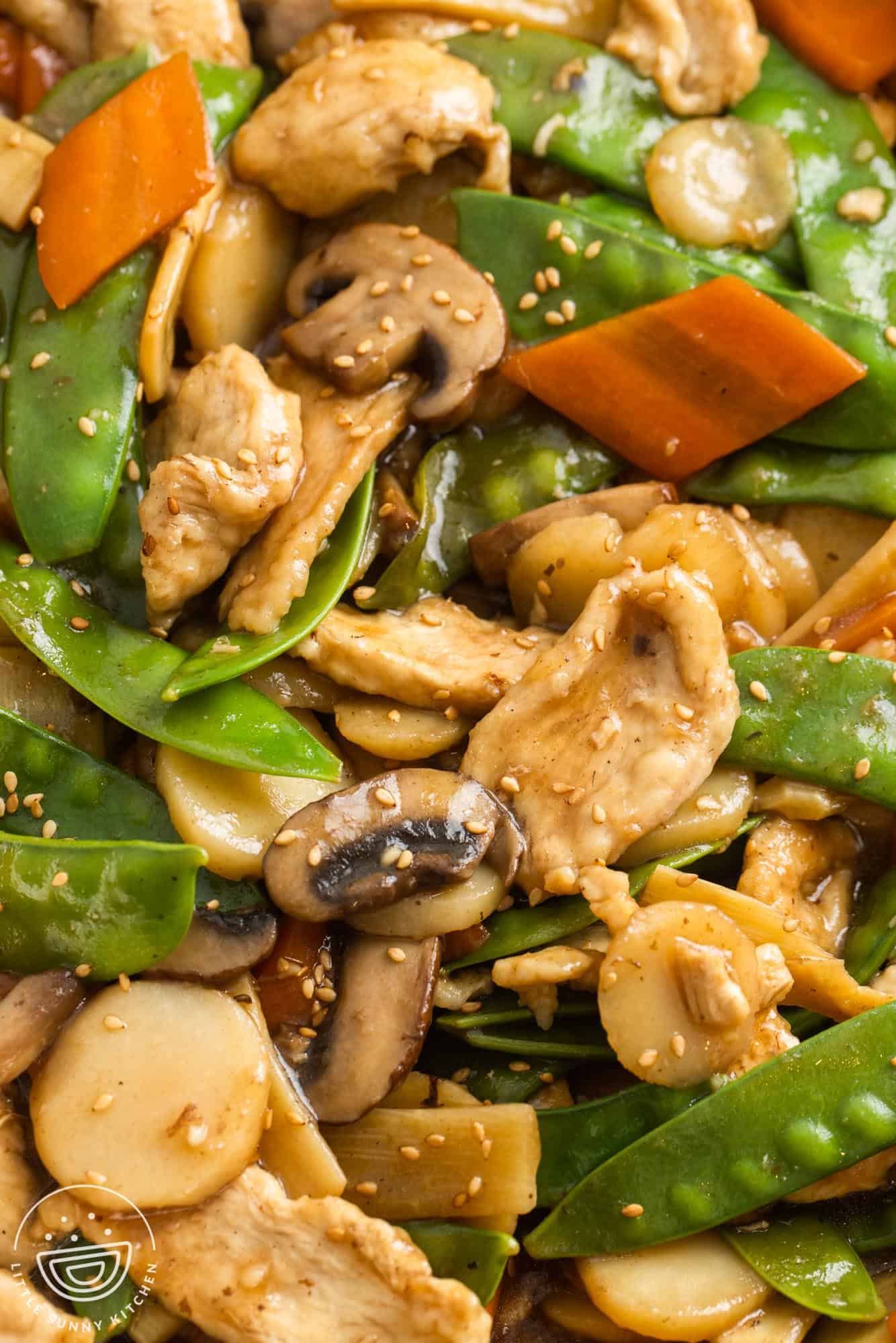 moo goo gai pan with veggies including snow peas, carrots, water chestnuts, and bamboo shoots, and sesame seeds.