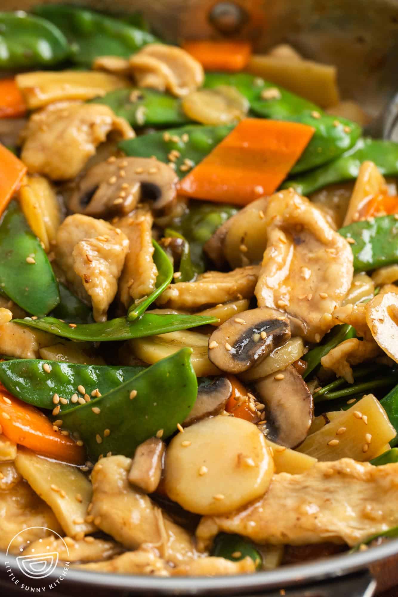 closeup of homemade moo goo gai pan with chicken, mushrooms, and snow peas, garnished with sesame seeds.