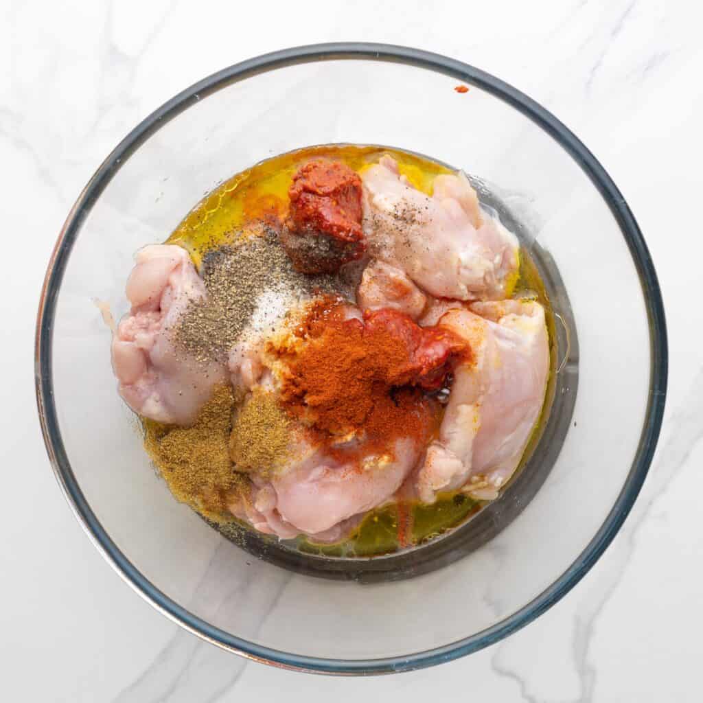 raw chicken thighs with Harissa seasonings in a glass bowl