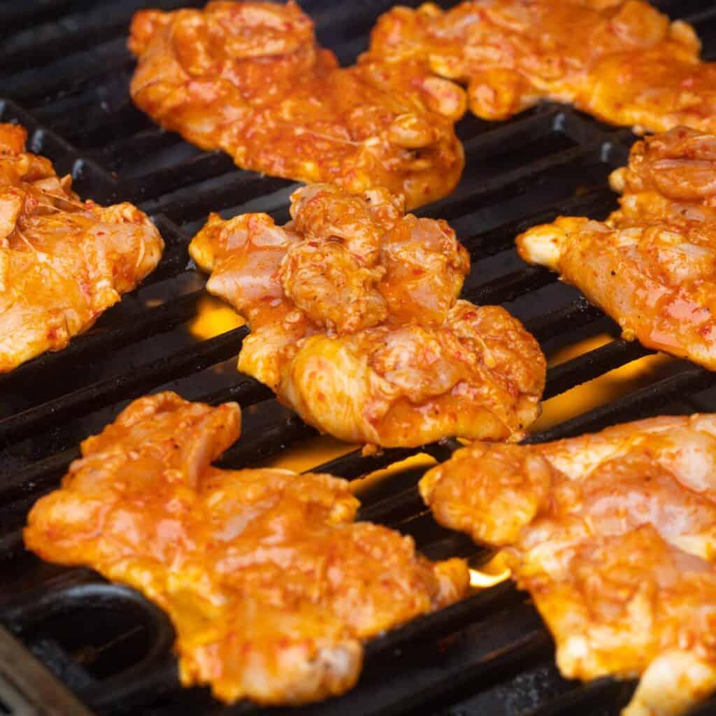 raw, marinated Harissa chicken thighs on a gas grill. 