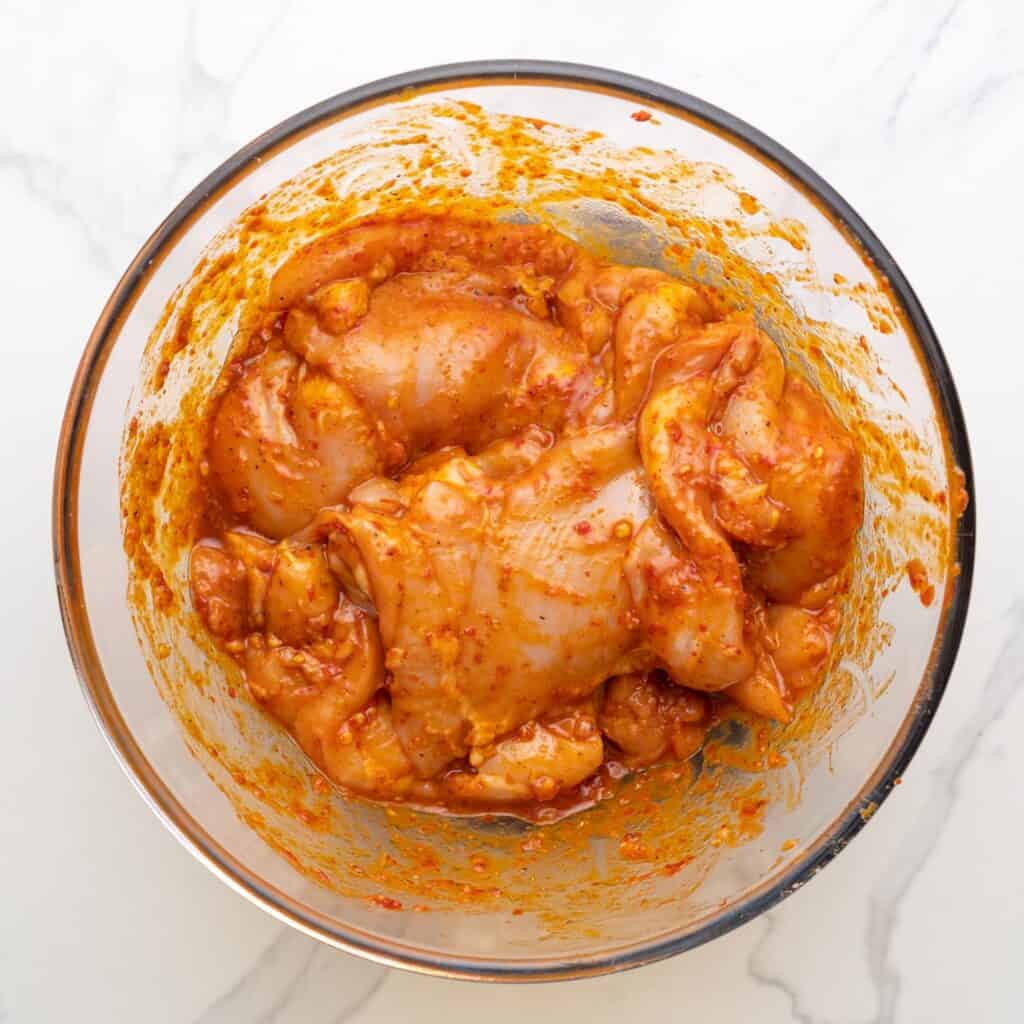 Marinated harissa chicken in a glass bowl, ready for grilling. 