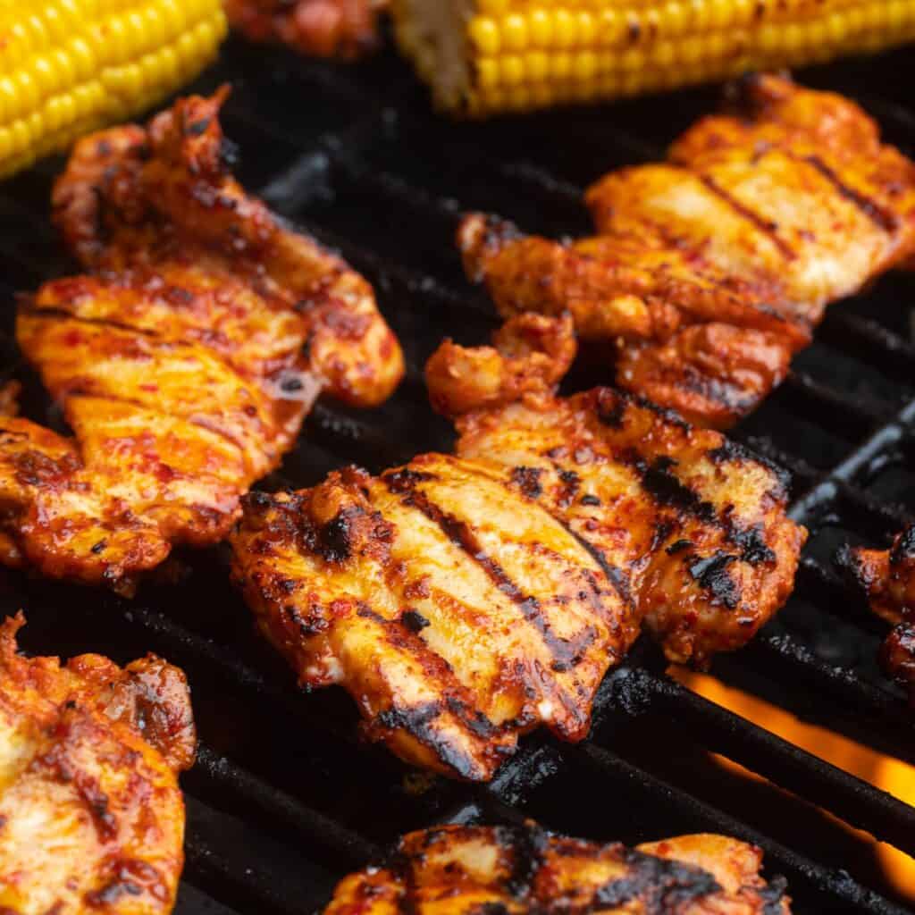 cooked grilled harissa chicken on a grill with corn on the cob.