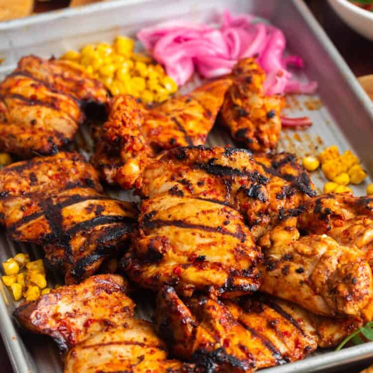 a sheet pan of grilled harissa chicken with onion and corn on the side.