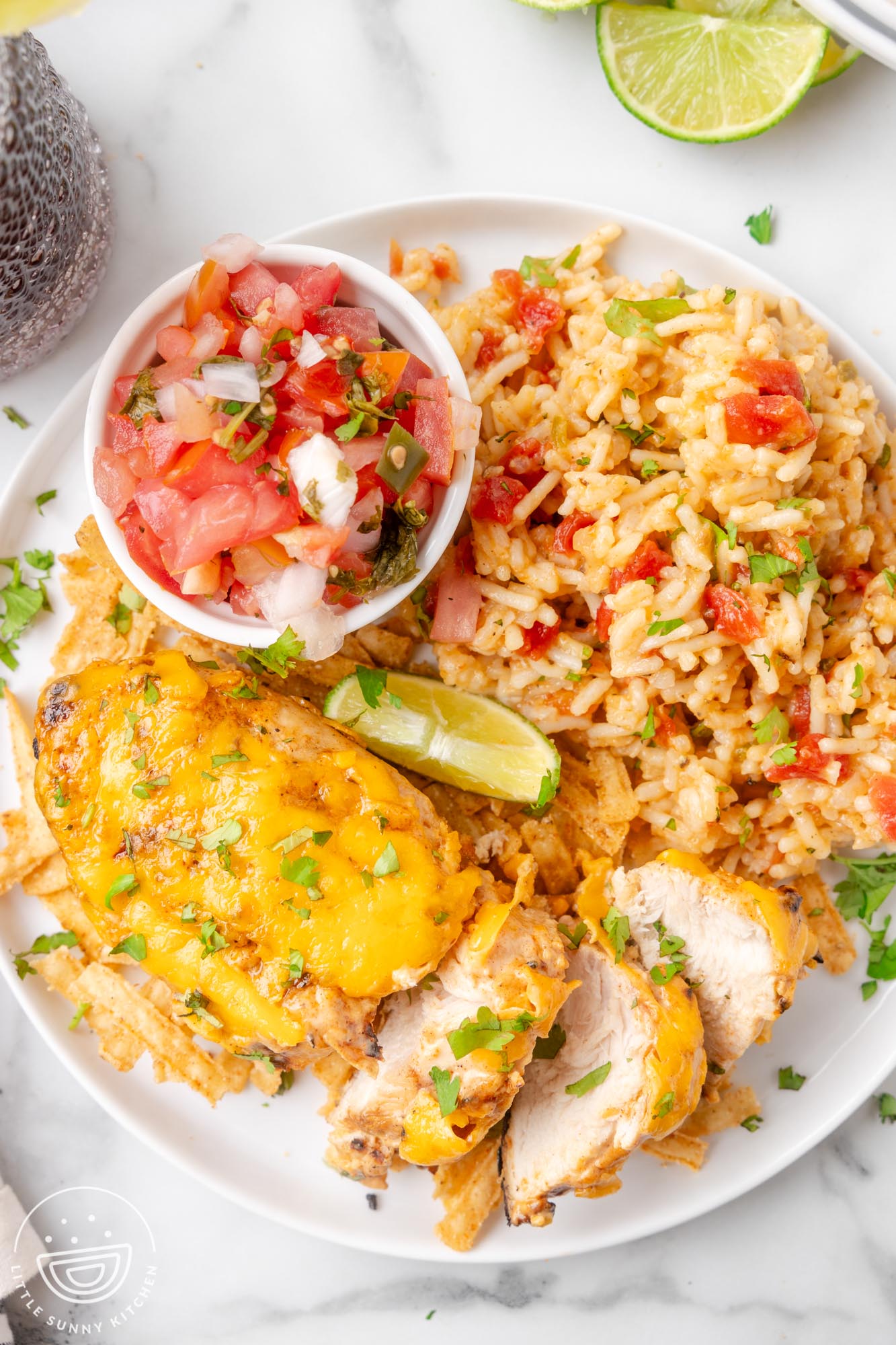 a white plate of sliced fiesta lime chicken, spanish rice, a lime wedge and a small bowl of pico de gallo.