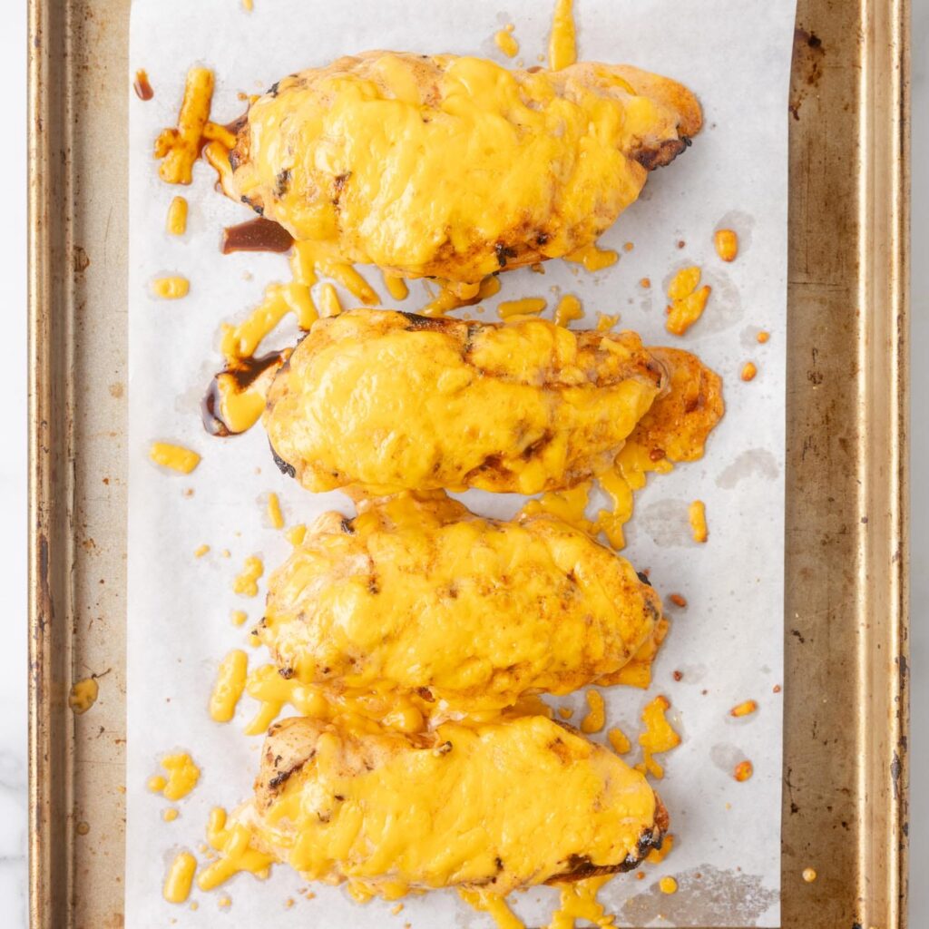 a sheet pan lined with parchment paper holding four chicken breasts smothered in cheese.